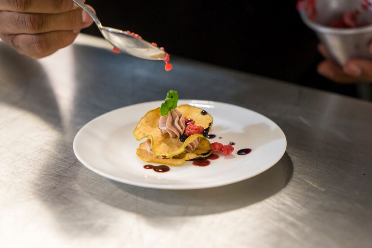 services-02 Close-up of a chef garnishing an elegant dessert with berry sauce on a white plate.